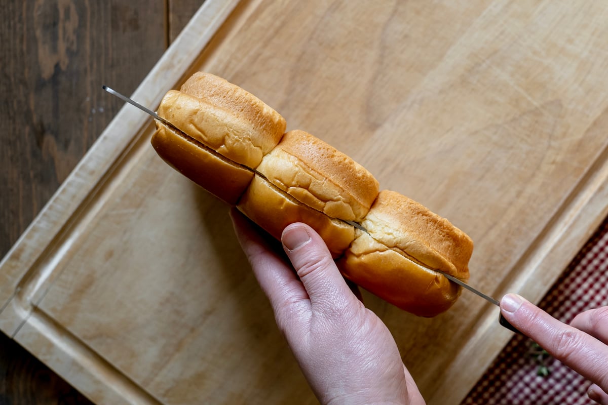 cutting brioche rolls in half for breakfast strata.