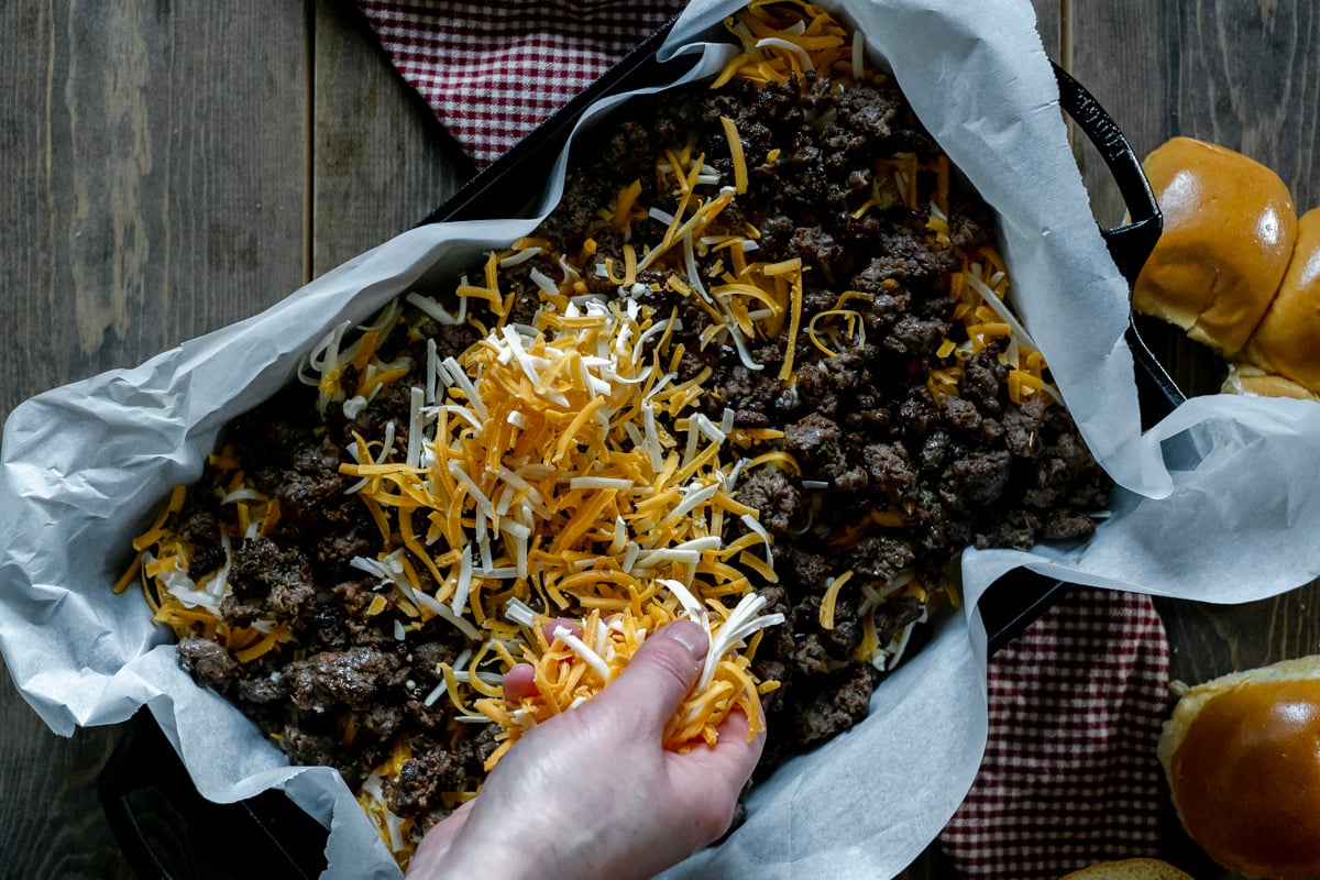 sprinkling cheese over sausage in casserole dish.