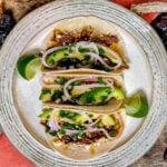 3 shredded venison tacos on white plate with lime wedges.