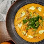 curry butternut squash soup with fresh toppings in black bowl.