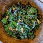 kale salad with walnuts and cherries in wood bowl.