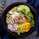 pheasant tom kha gai in wood bowl with fresh toppings.