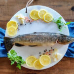 trout on marble plate with lemon slices and herbs.