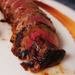 venison eye of round sliced on white tray.