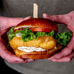 hands holding beer-battered halibut sandwich.