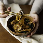 hand holding chopsticks of elk pad see ew above bowl.