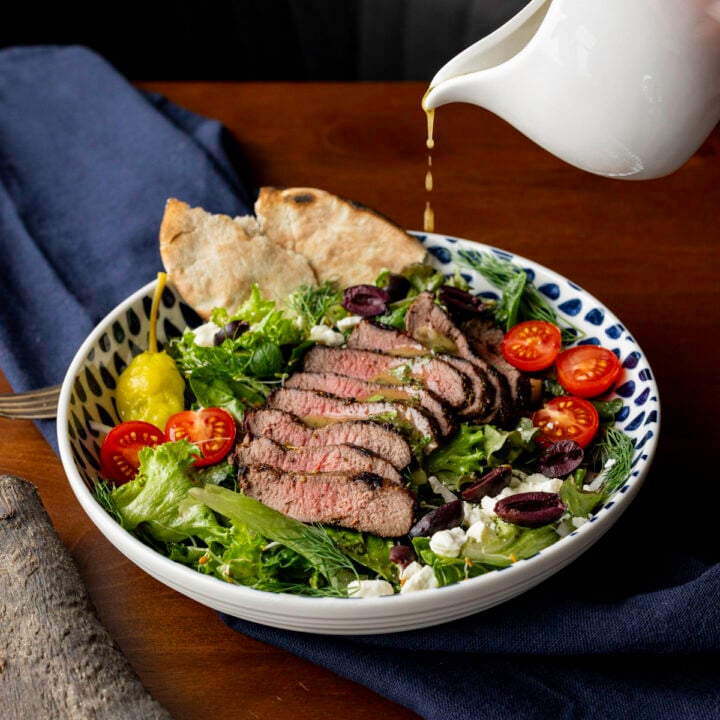 pouring Greek salad dressing over antelope steak salad.