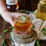 hand lifting glass with spruce tip old fashioned.