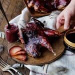 hand holding board with grilled chukar with plum sauce.