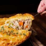 hand pulling piece of rabbit pot pie out of pie pan.