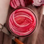 sliced pickled red onions in jar on purple cloth.