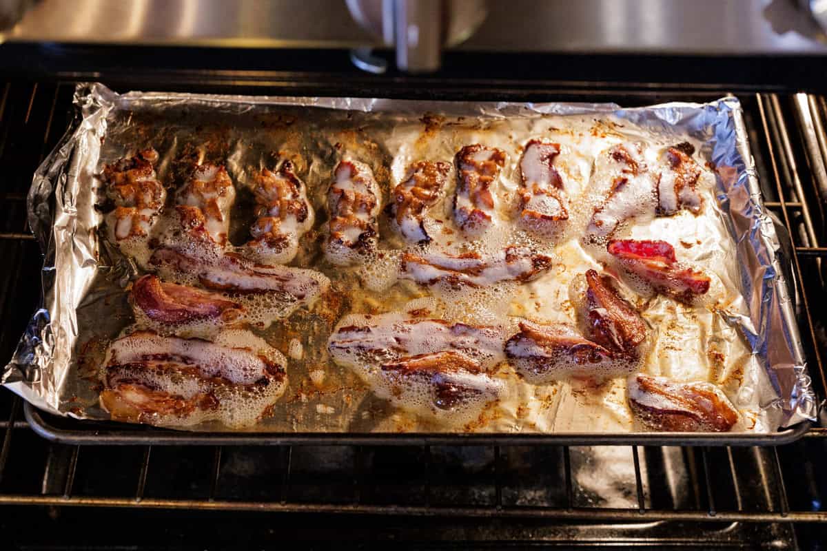 bacon slices cooking in oven on sheet pan.
