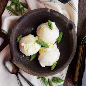 Three scoops of ice cream in a bowl with spruce tips.