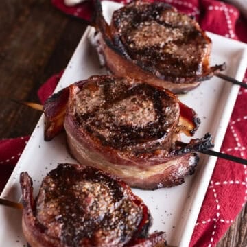 3 bacon-wrapped venison backstrap medallions on white plate.
