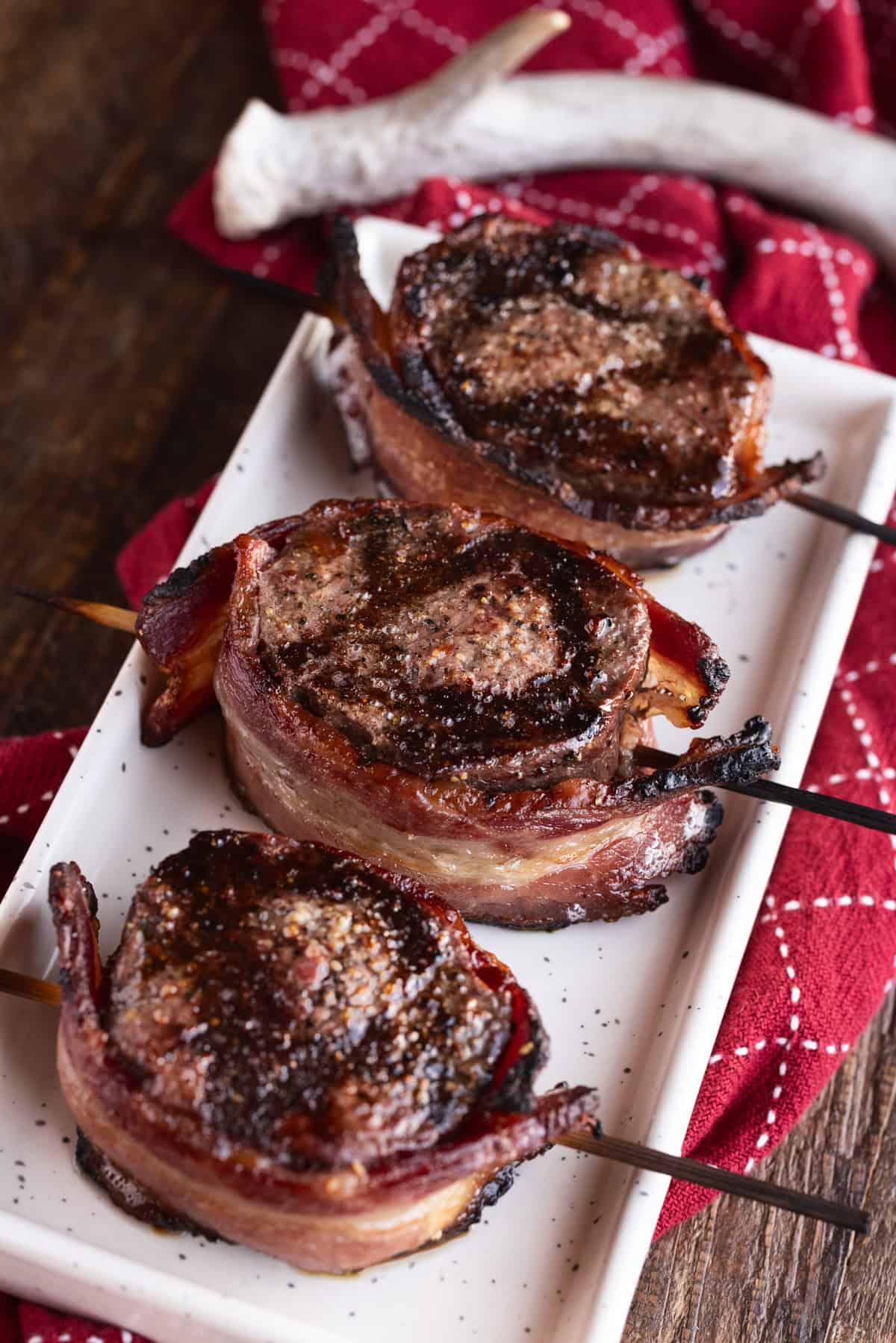 3 bacon-wrapped venison backstrap medallions on white plate.