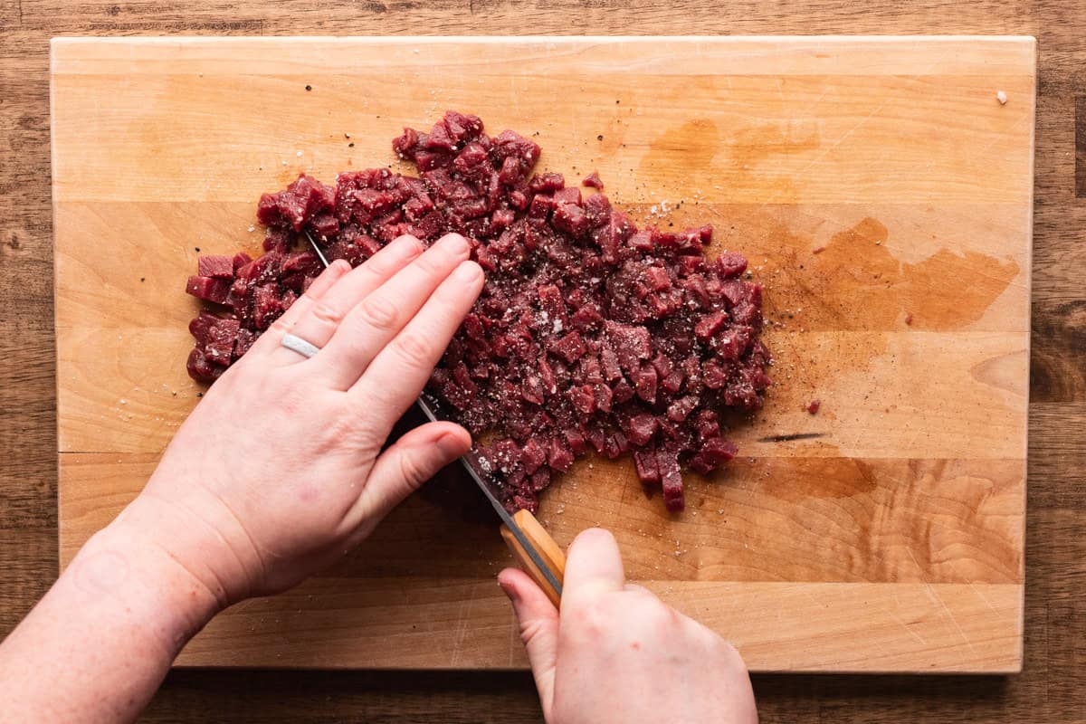 chopping venison for tartare on cutting board.