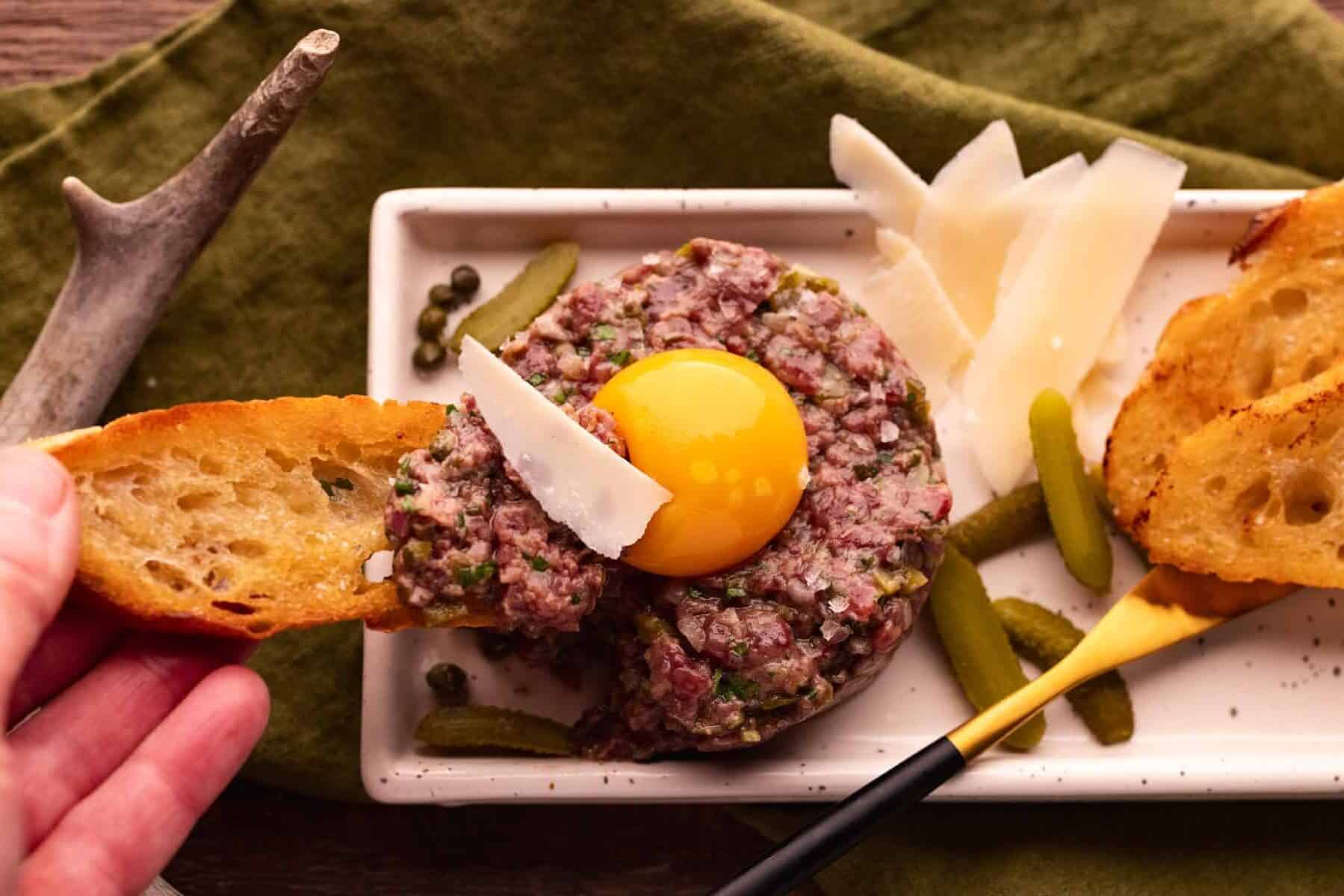 dipping baguette with venison tartare in egg yolk.