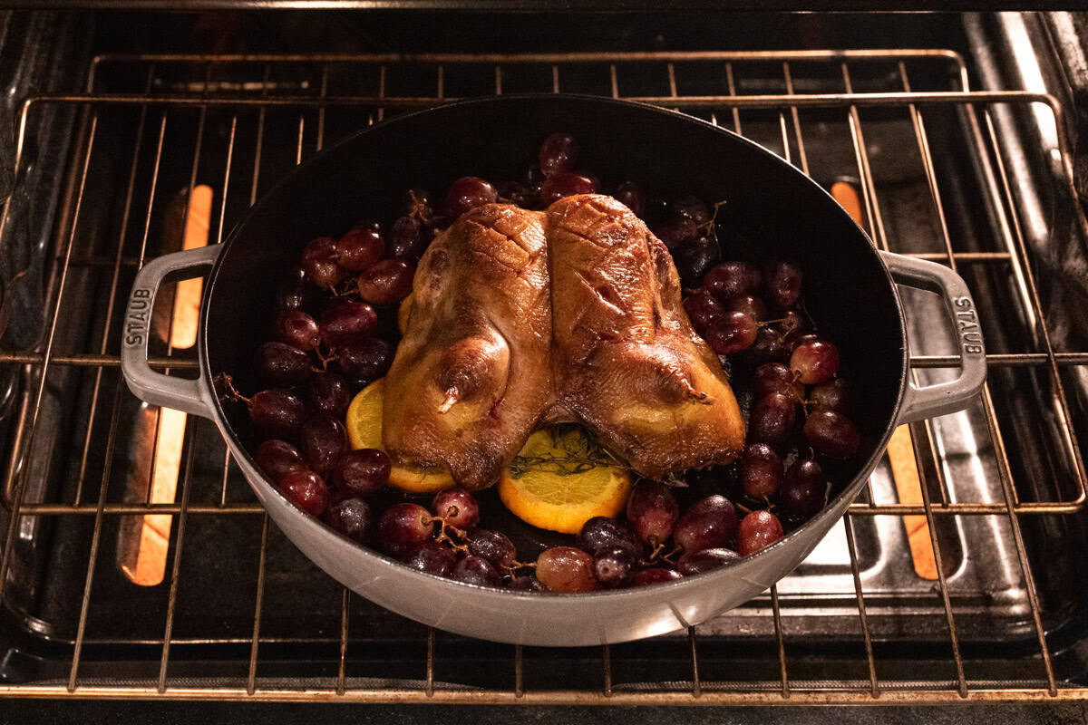 duck roasting in oven with grapes.