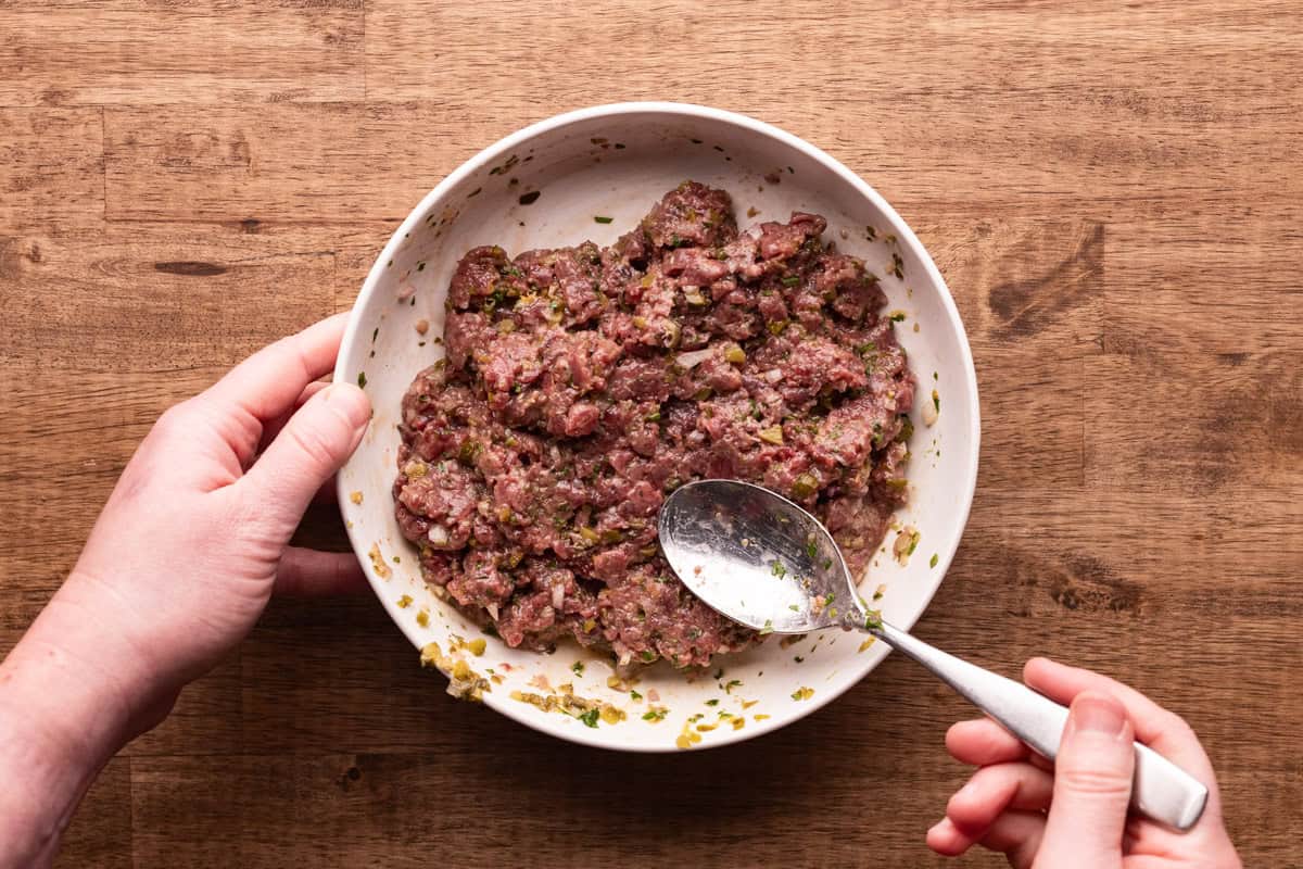 mixing venison tartare in bowl.