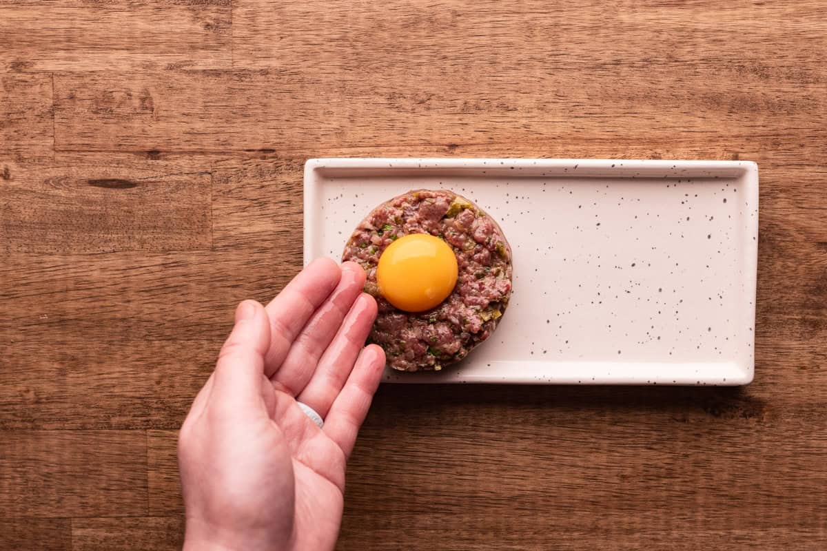 placing egg yolk on venison tartare.