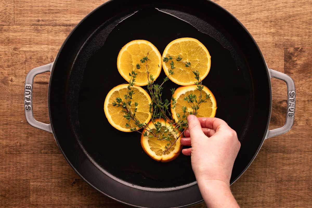 placing thyme and orange slices in cast iron pan.