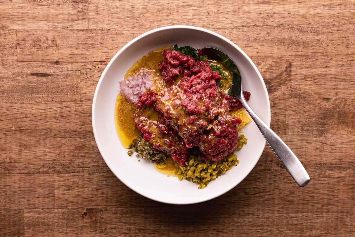 venison tartare ingredients with sauce in bowl.