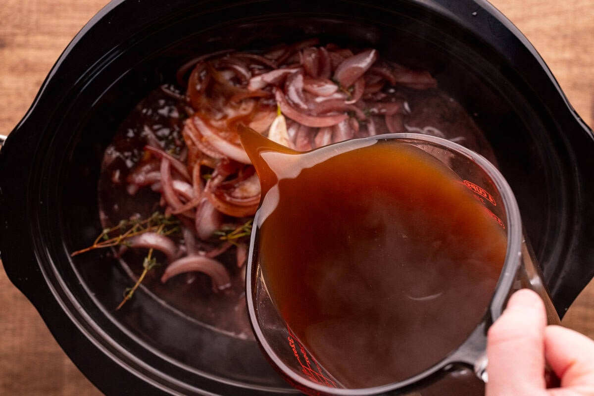 pouring broth into crock pot with elk roast.