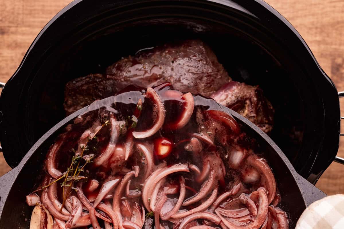 pouring onions and red wine into crock pot with elk roast.