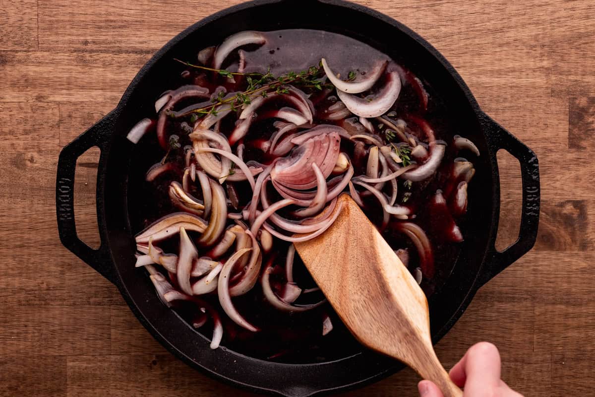 stirring onions with red wine in cast iron skillet.