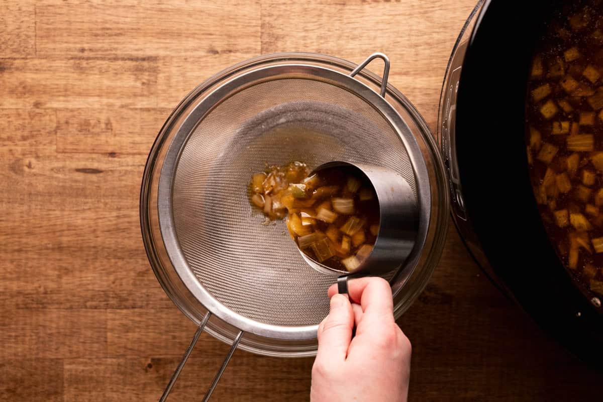 pouring carnitas liquid through strainer.