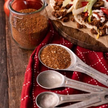 taco seasoning in measuring spoons with tacos in background.