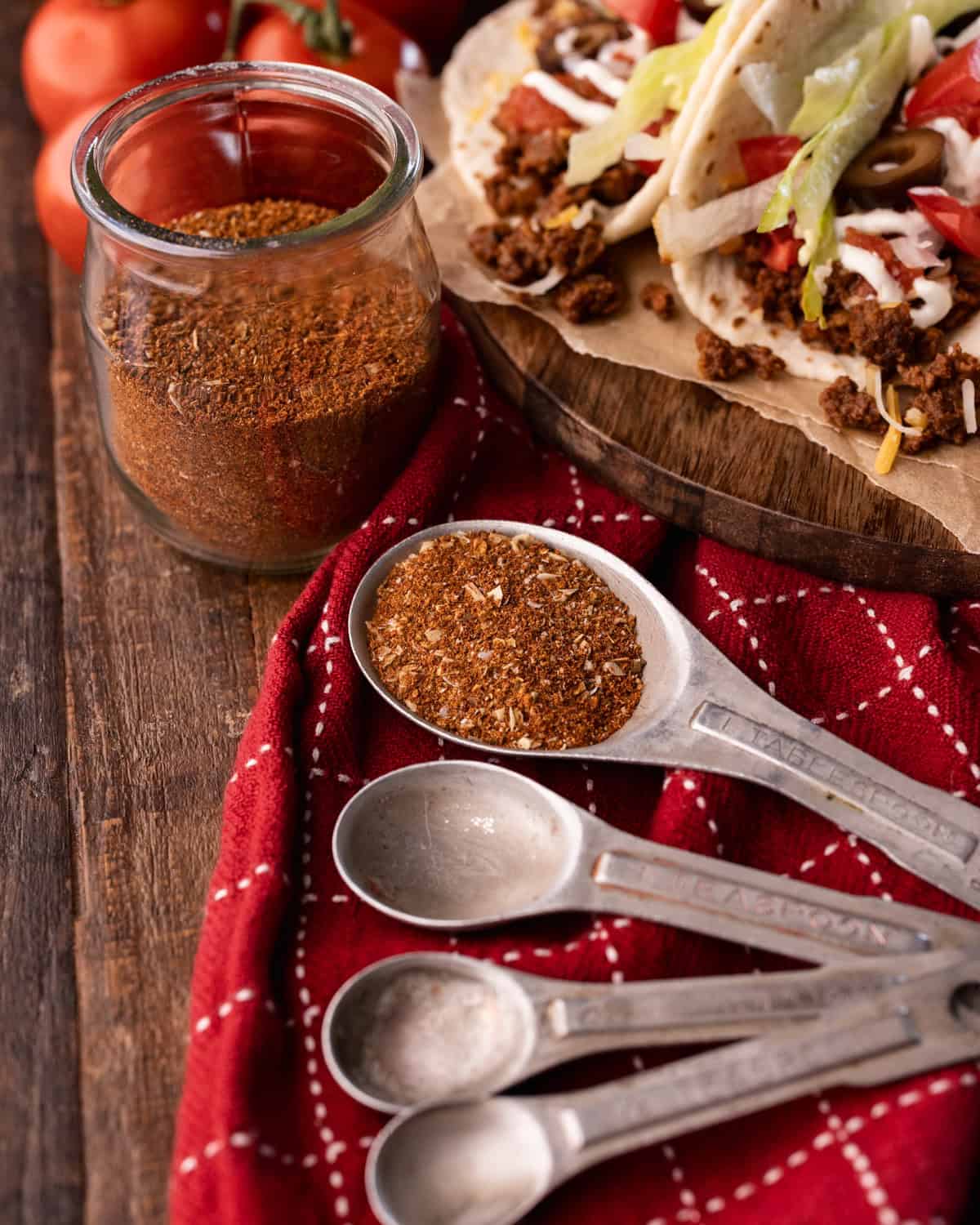taco seasoning in measuring spoons with tacos in background.