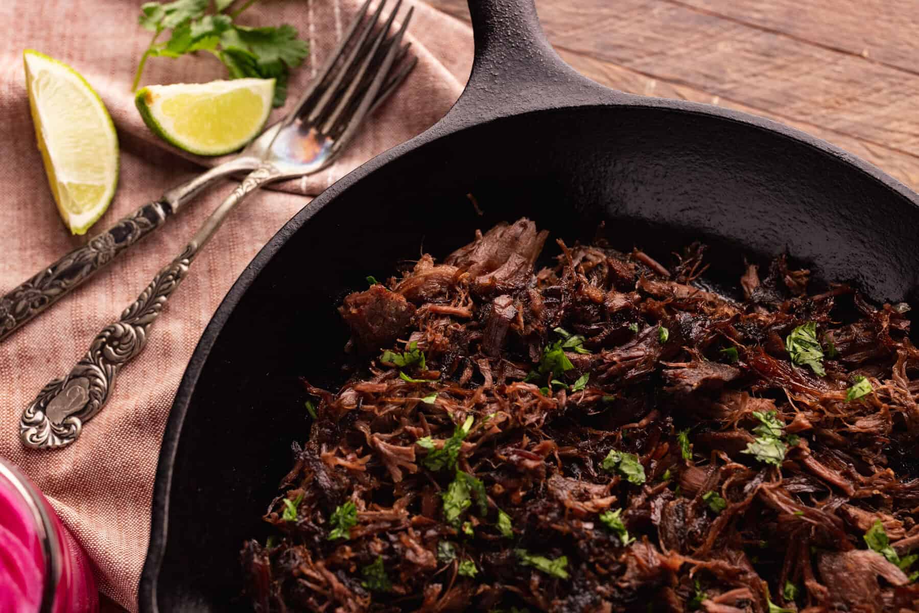 venison shank carnitas in skillet with limes.
