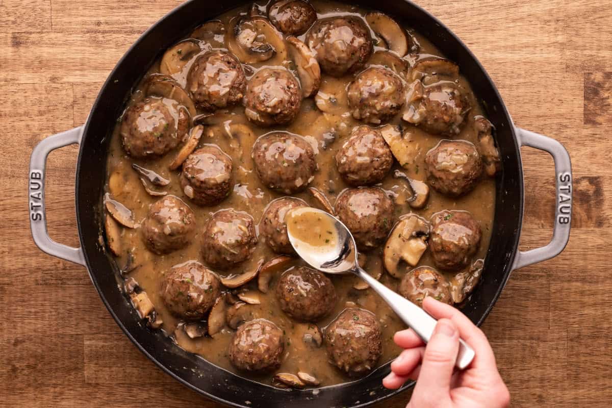 spooning sauce over meatballs in pan.