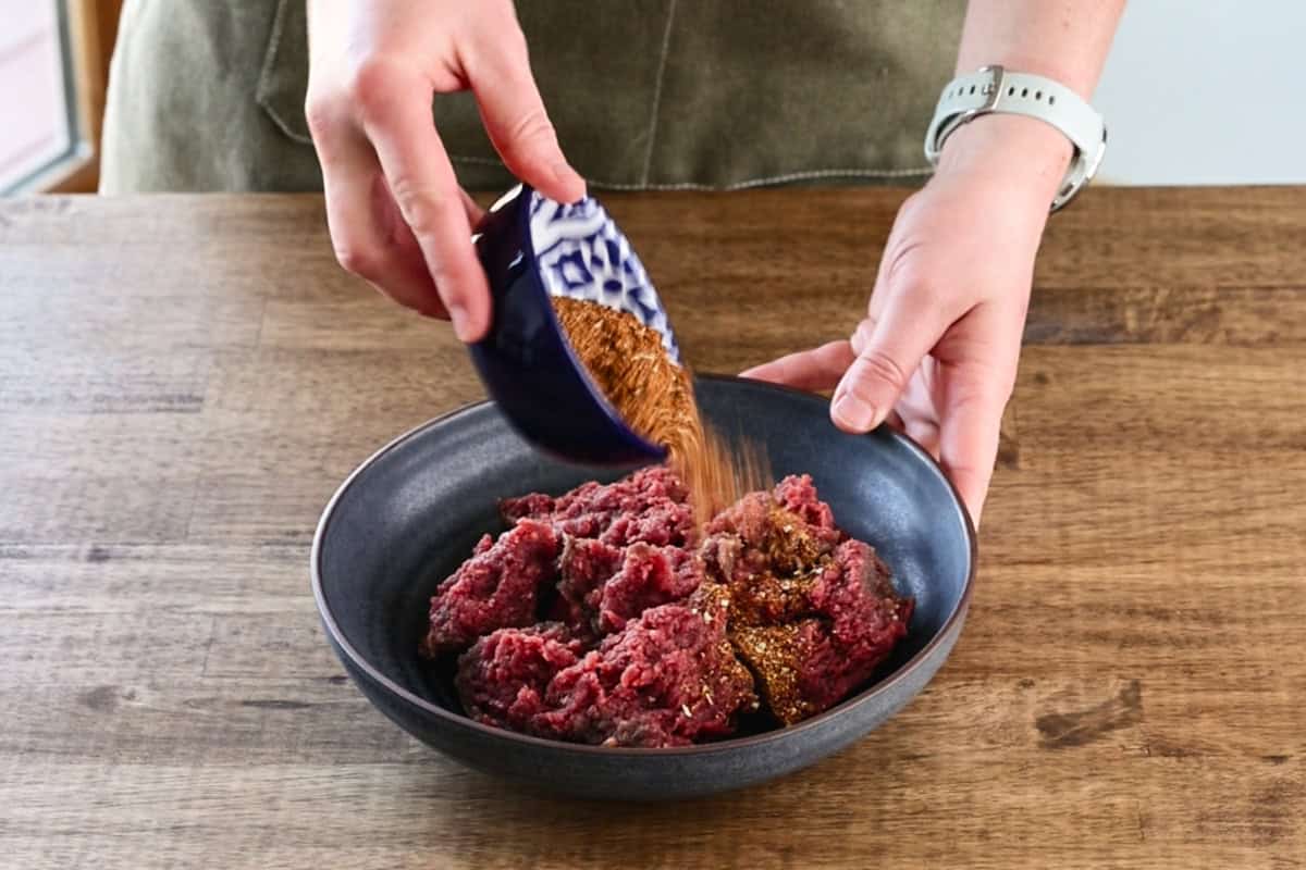 pouring taco seasoning over ground venison.