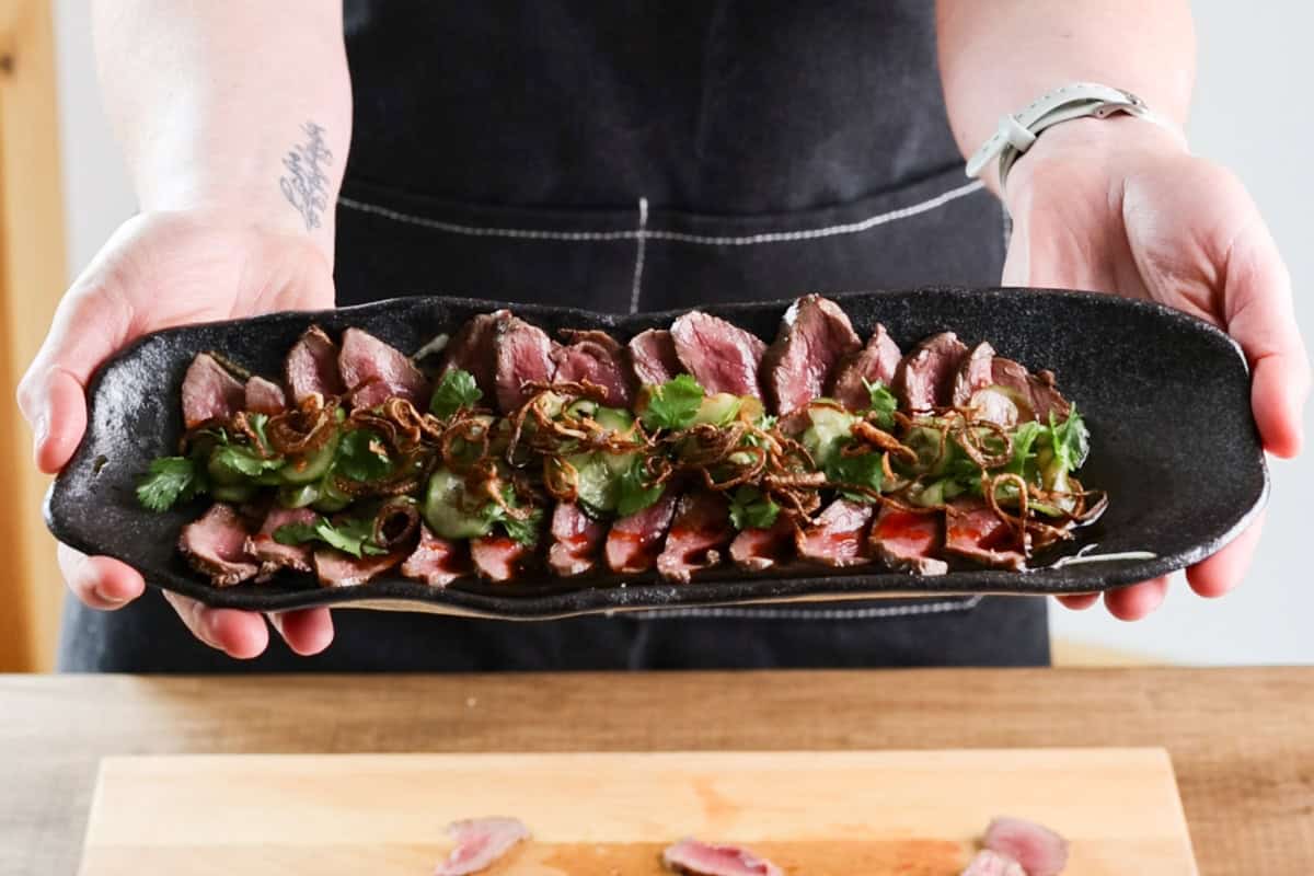 hands holding serving dish with venison tataki.
