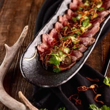 slices of venison tataki on black serving dish.