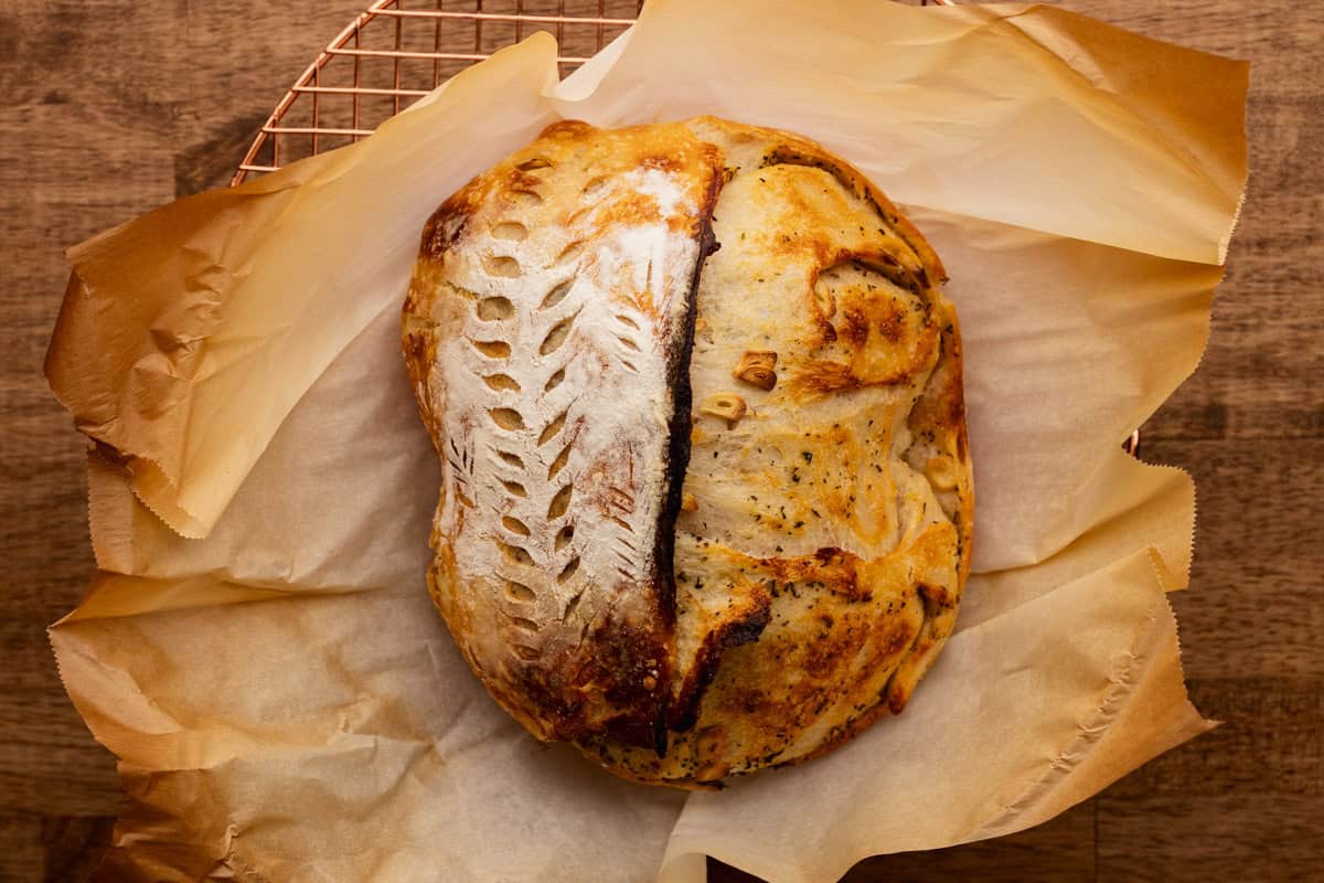 baked garlic and herb sourdough loaf on parchment.