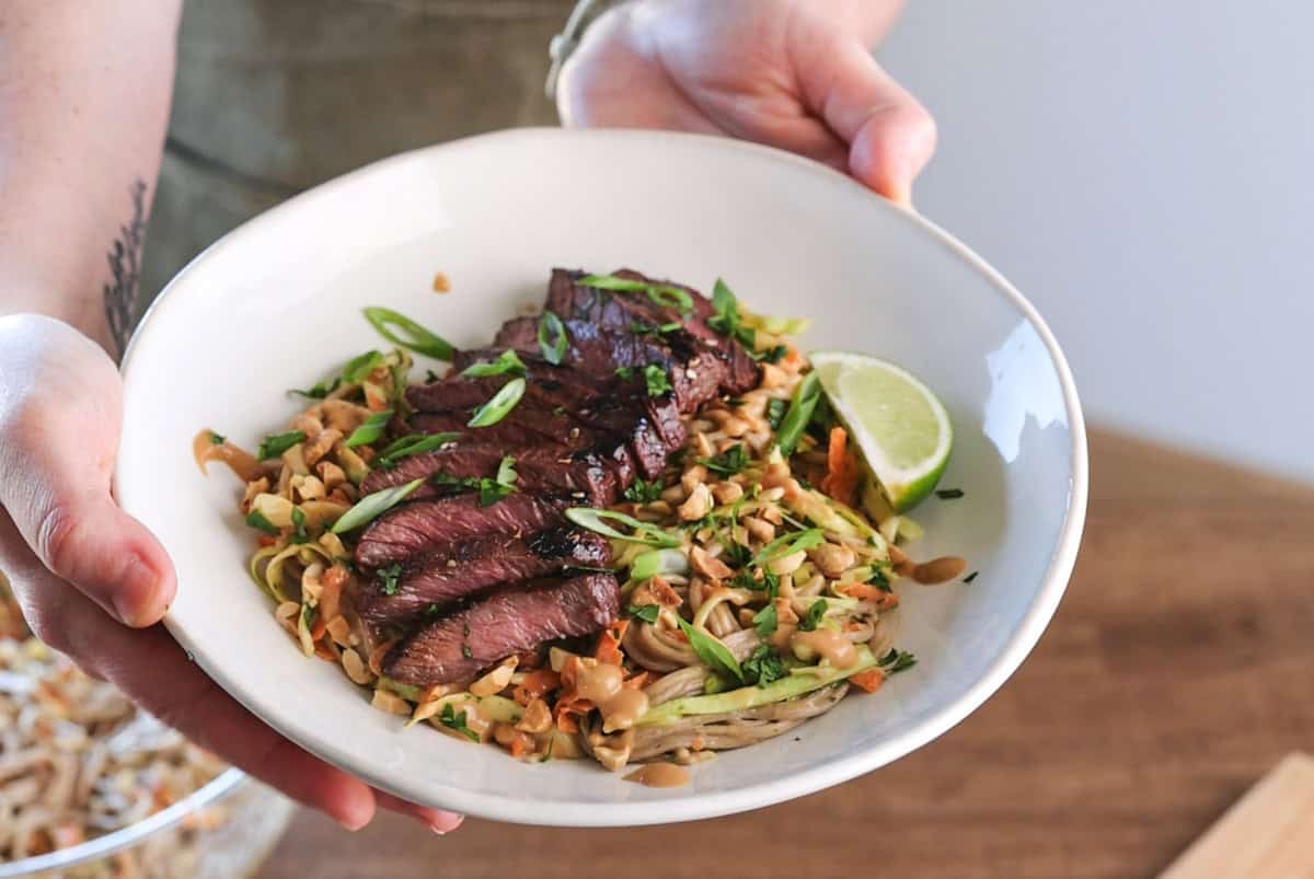 hands holding elk steak noodle bowl with peanut sauce.