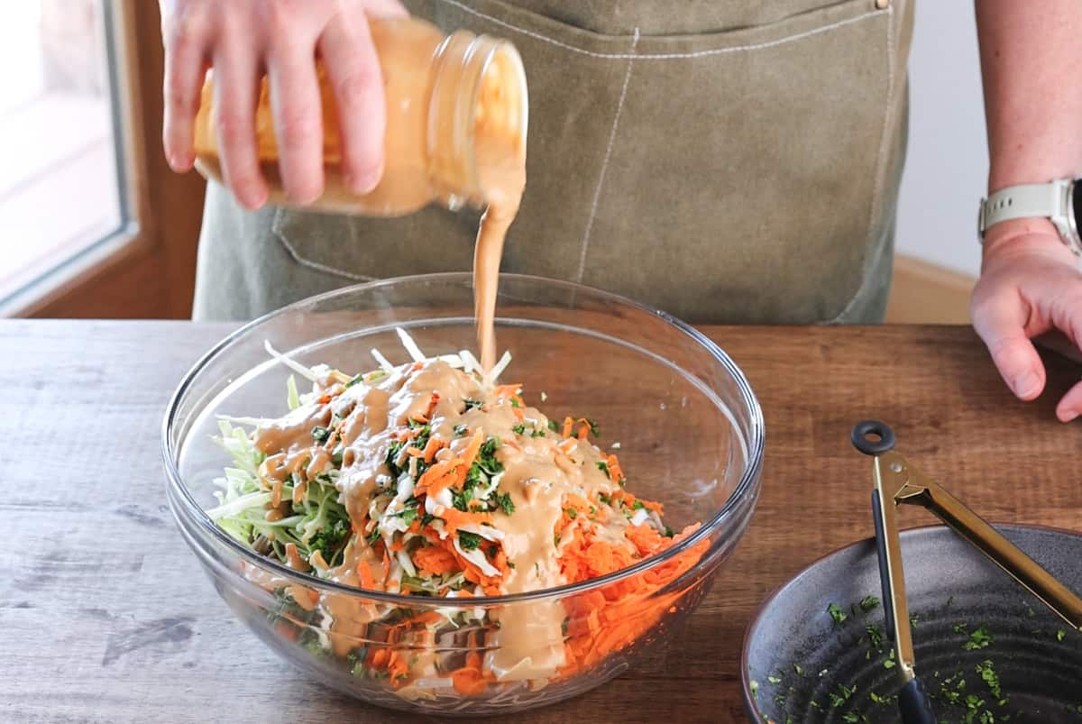 pouring peanut sauce over bowl with soba noodles and vegetables.