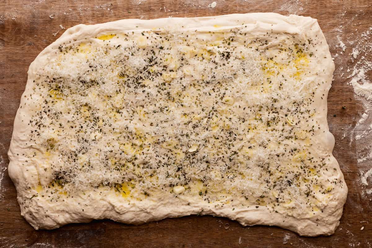 sourdough dough rectangle with olive oil, garlic, cheese, and herbs.