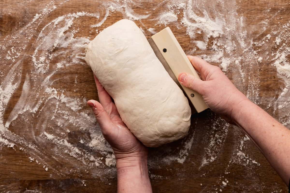 using bench scraper to tighten edges of sourdough loaf.